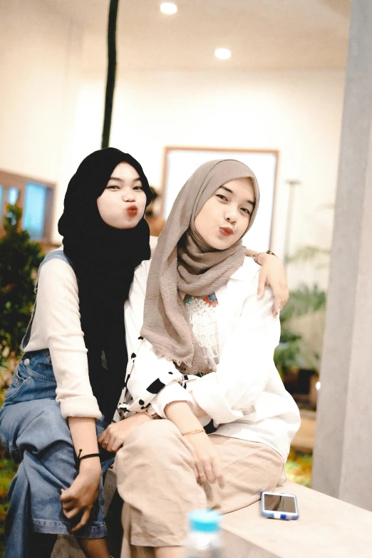 two women sitting next to each other on a bench, a picture, inspired by JoWOnder, trending on pexels, realism, white hijab, large lips, two buddies sitting in a room, photo booth