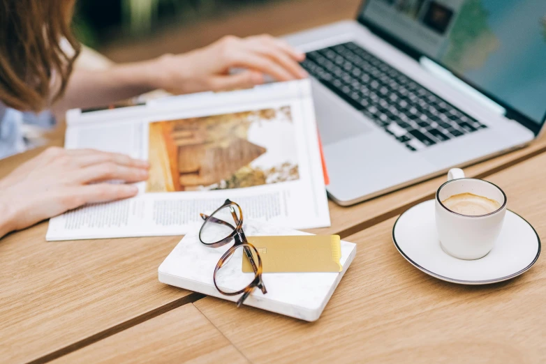 a woman sitting at a table with a laptop and a cup of coffee, a picture, by Daniel Gelon, pexels contest winner, white reading glasses, brochure, 9 9 designs, tourist photo