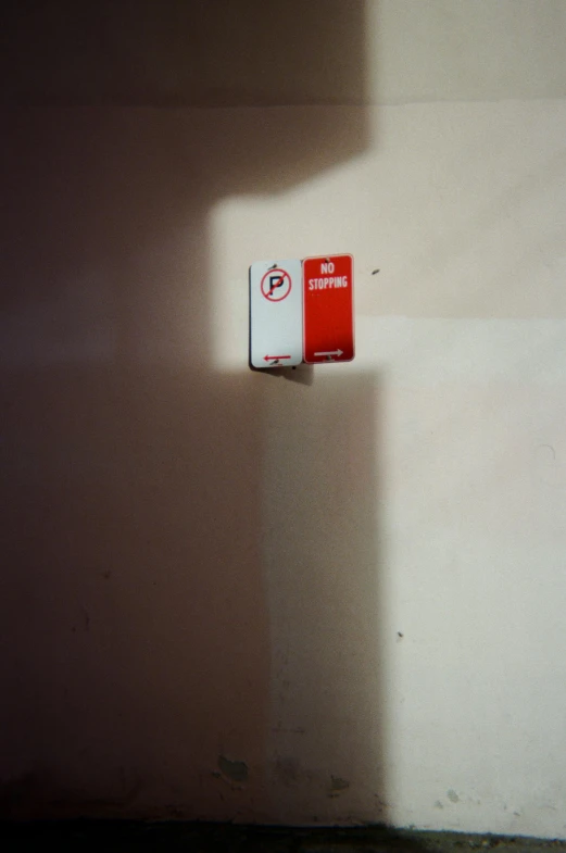 a red and white sign sitting on the side of a wall, a picture, unsplash, postminimalism, cigarette dangling, single point of light, white box, fujifilm superia
