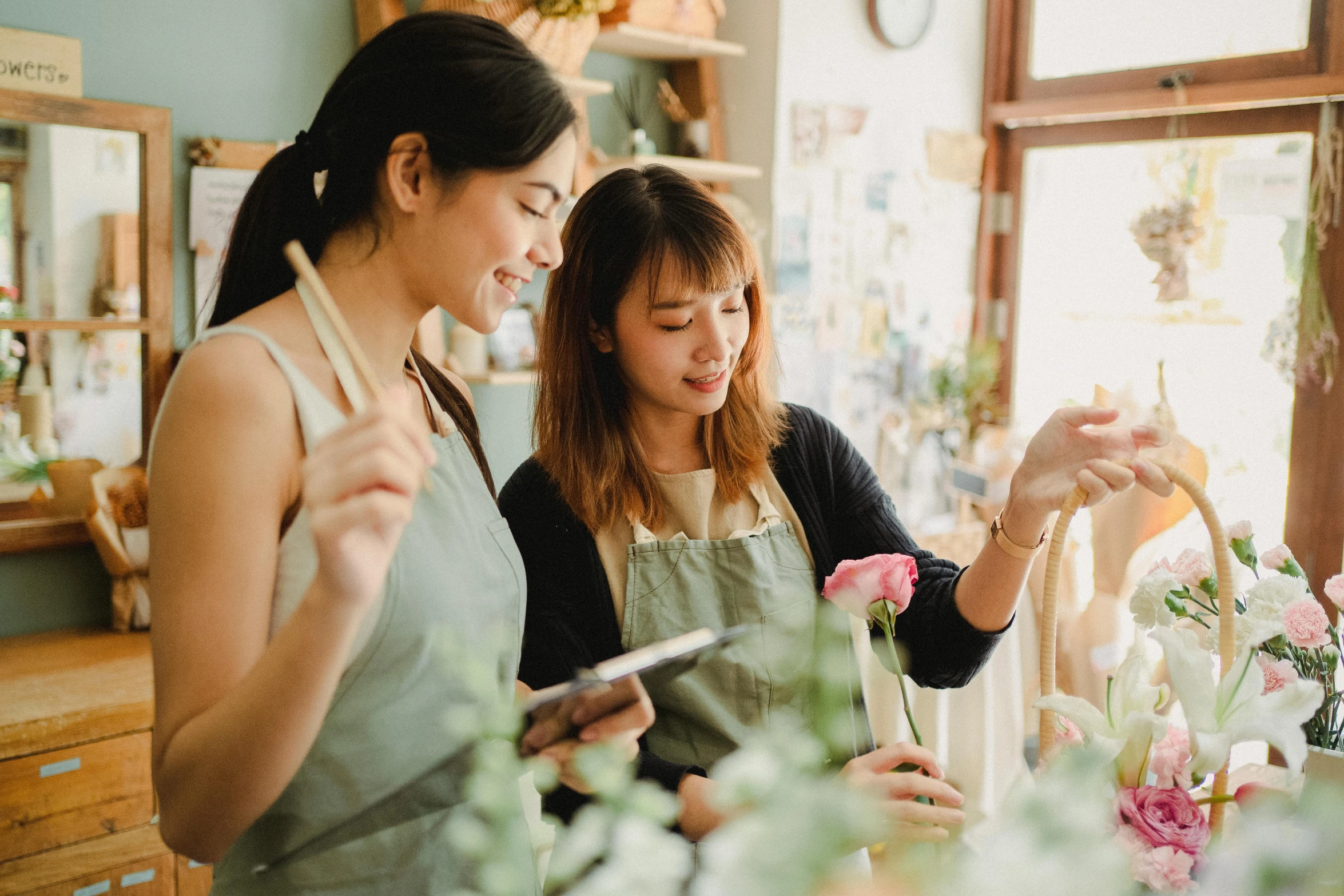 a couple of women standing next to each other in a room, a picture, pexels contest winner, arts and crafts movement, flower shop scene, avatar image, asian female, writing on a clipboard