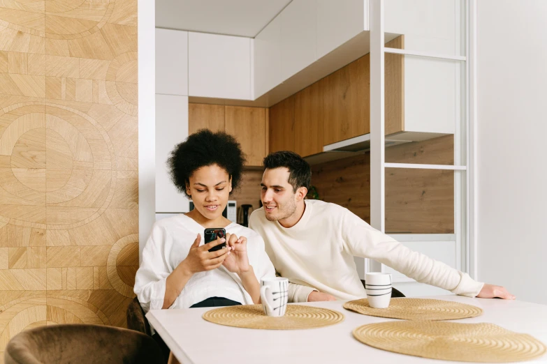 a man and woman sitting at a table looking at a cell phone, pexels contest winner, modernism, brown and white color scheme, apartment, sleek design, delightful