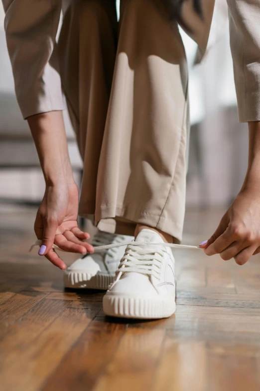 a woman tying her shoes on a hard wood floor, inspired by Elsa Bleda, trending on pexels, renaissance, wearing white suit, wearing adidas clothing, coat pleats, khakis