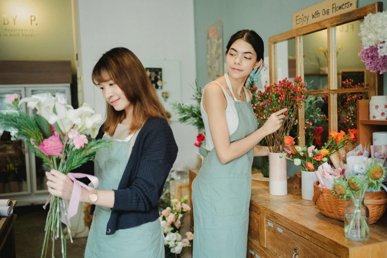 a woman standing next to another woman in a flower shop, trending on pexels, animation, asian female, wearing overalls, vase work