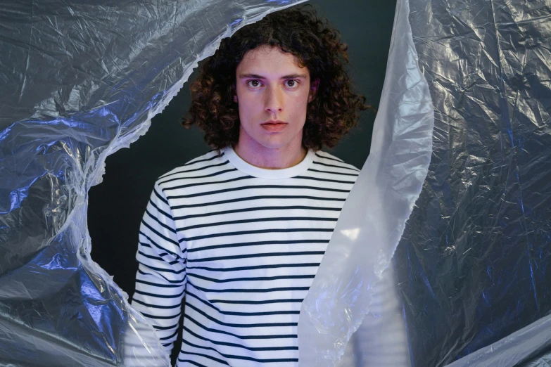 a man with curly hair wearing a striped shirt, an album cover, by Adam Dario Keel, pexels contest winner, wearing a plastic garbage bag, blank stare”, in a claustrophobic, male model