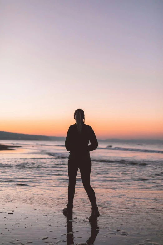 a woman standing on top of a beach next to the ocean, during a sunset, profile image