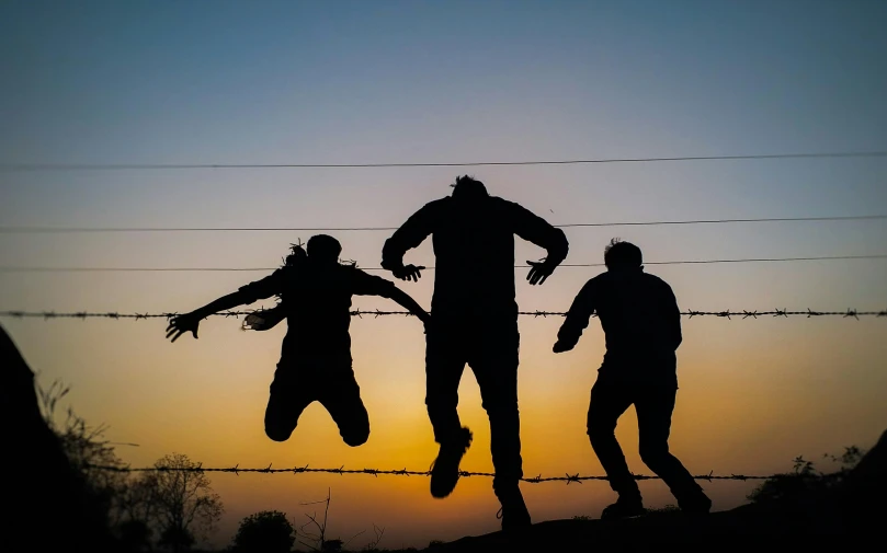 a group of people that are jumping in the air, by Jesper Knudsen, pexels contest winner, barbed wire, backlit, friendship, 15081959 21121991 01012000 4k