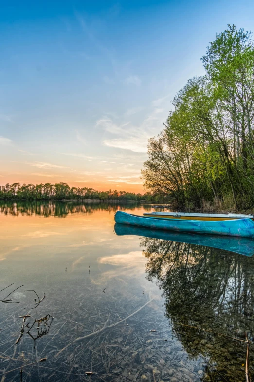 a blue boat sitting on top of a lake, by Paweł Kluza, at sunrise in springtime, today\'s featured photograph 4k, fine art print, wide angle river