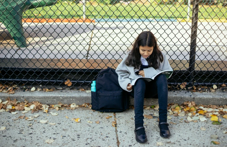 a little girl sitting on the ground reading a book, a picture, pexels contest winner, american barbizon school, in an urban setting, humans of new york, school bag, snapchat photo