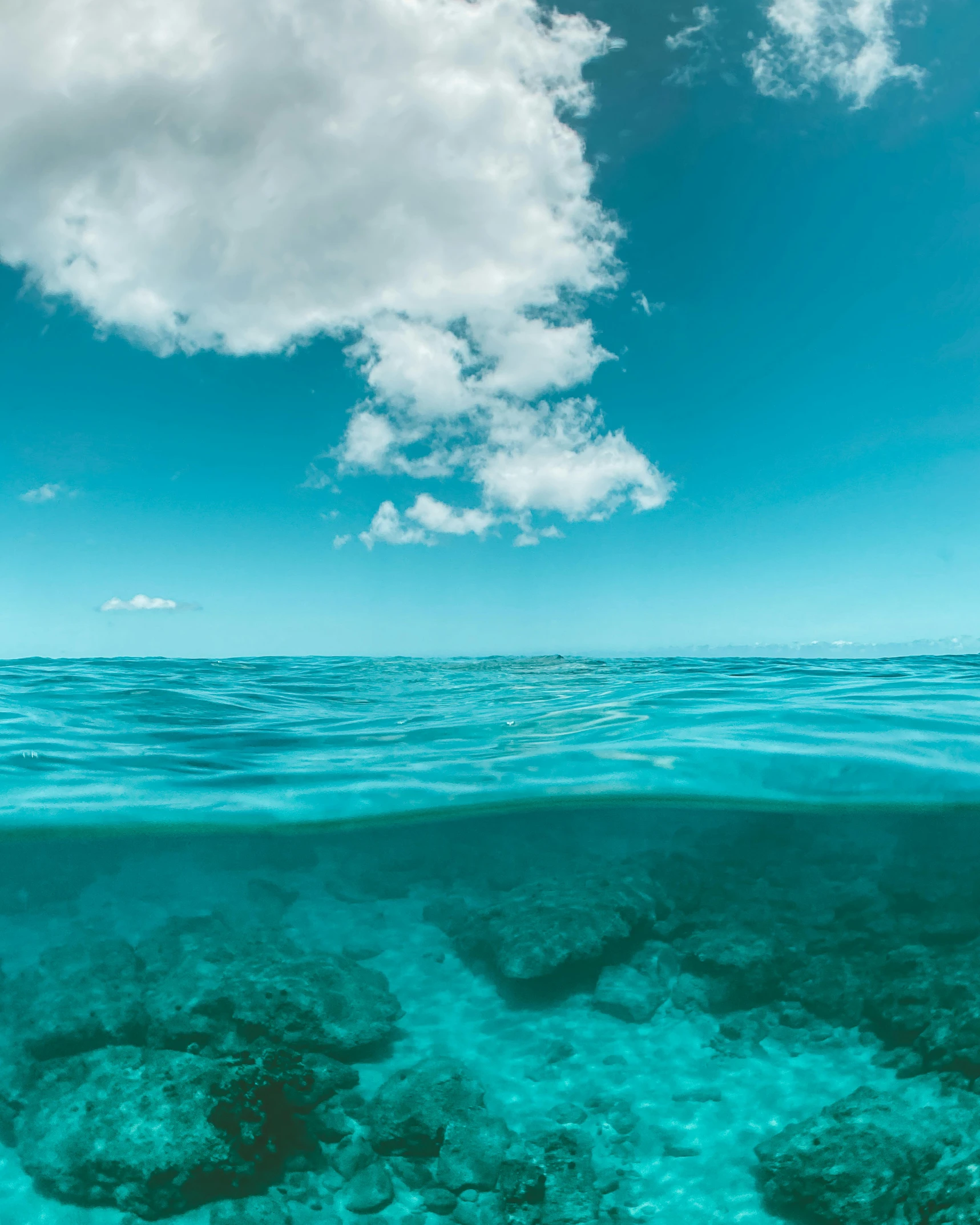 a view of the ocean from the bottom of the water, standing beside the ocean, clouds on surface, sapphire waters below, taken in 2 0 2 0