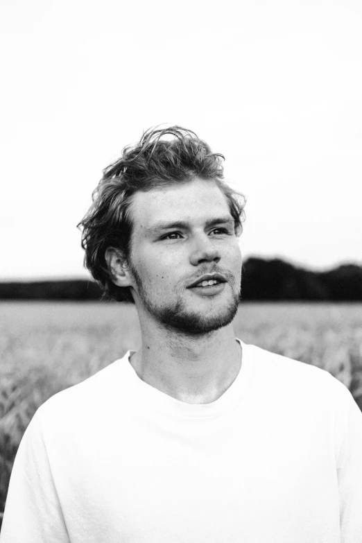 a black and white photo of a man in a field, a black and white photo, inspired by Samu Börtsök, unsplash, orelsan, headshot profile picture, dressed in a white t-shirt, homelander