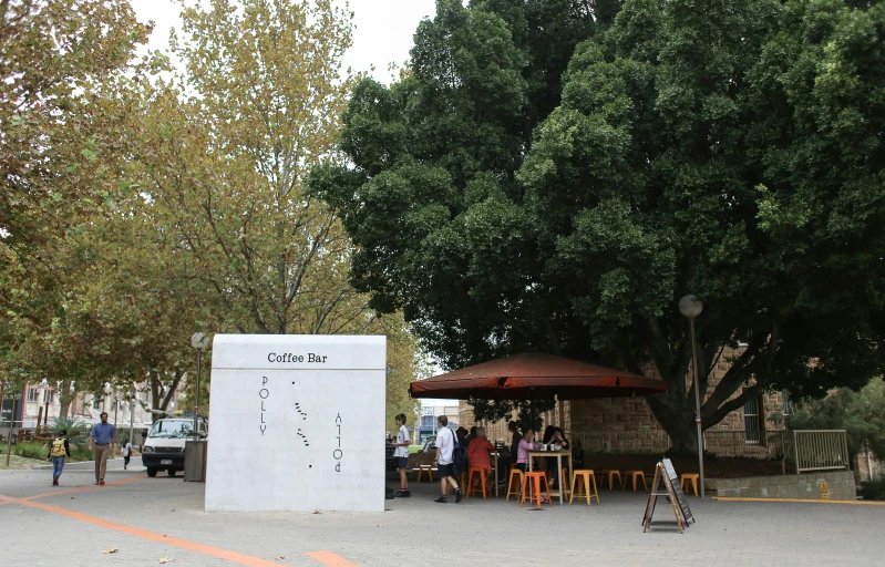 a white sign sitting on the side of a road, by Michael Goldberg, temporary art, cafe tables, huge central tree, rammed earth courtyard, the cube