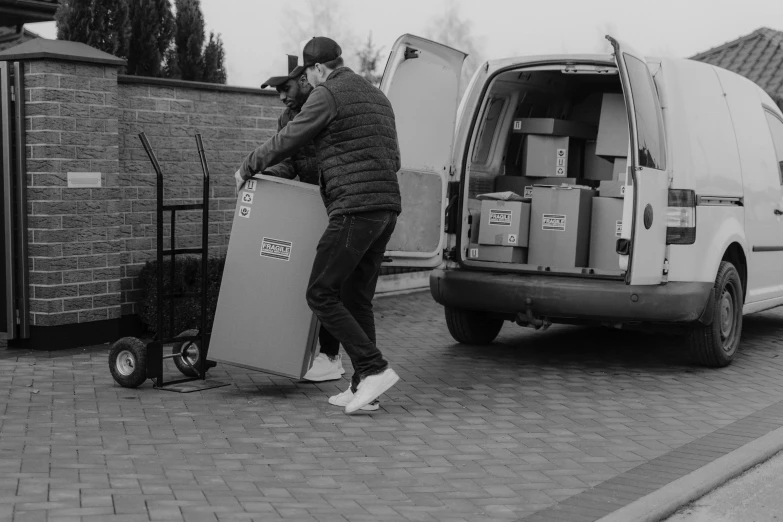 a black and white photo of a man loading boxes into a van, by Adam Marczyński, pexels contest winner, low quality footage, cart, avatar image, outdoor photo
