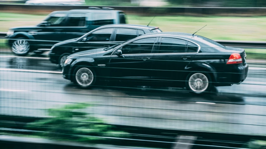 a couple of black cars driving down a street, unsplash, photorealism, panning shot, accompanying hybrid, car on highway, gm