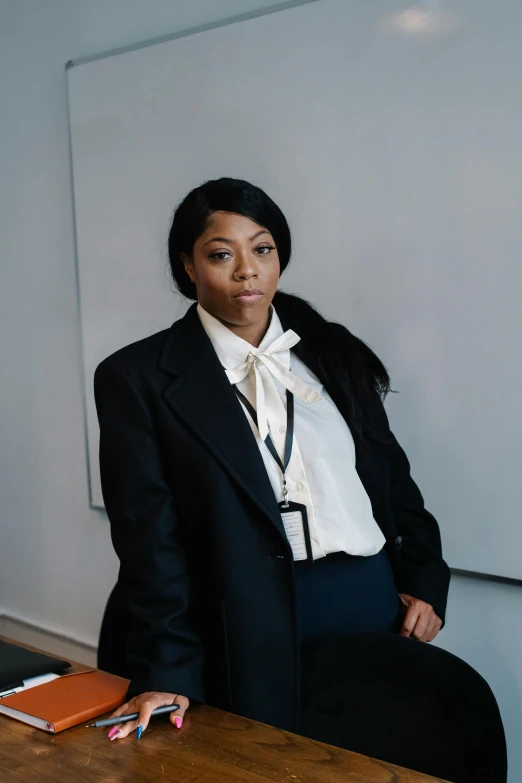 a woman sitting at a table in front of a whiteboard, by Thomas Fogarty, black business suit, wearing headmistress uniform, moody light, naomi campbell