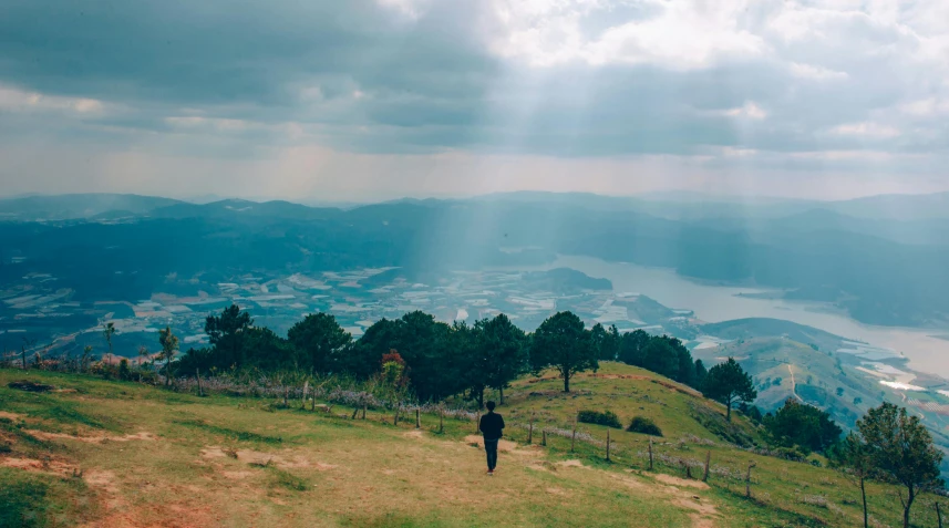 a man standing on top of a lush green hillside, pexels contest winner, sumatraism, guwahati, panoramic view of girl, walking away, some sunlight ray