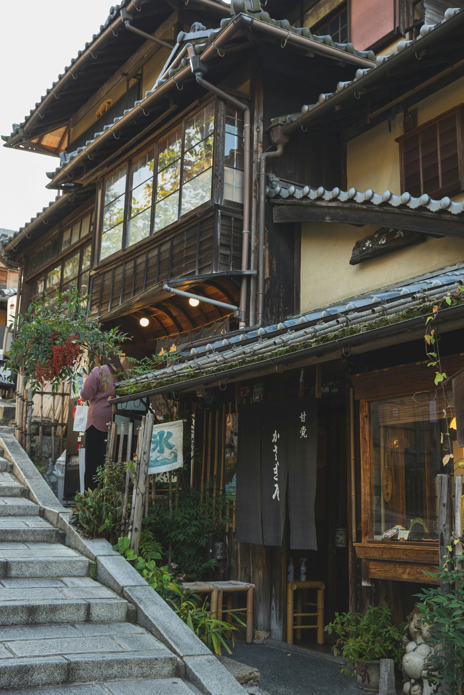 a person walking up a set of stairs in front of a building, inspired by Tōshi Yoshida, trending on unsplash, ukiyo-e, a multidimensional cozy tavern, peaked wooden roofs, preserved historical, large overhangs