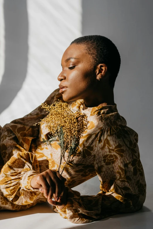 a woman sitting on the floor with a flower in her hand, trending on unsplash, renaissance, in a gold suit, brown buzzcut, roots and hay coat, young black woman