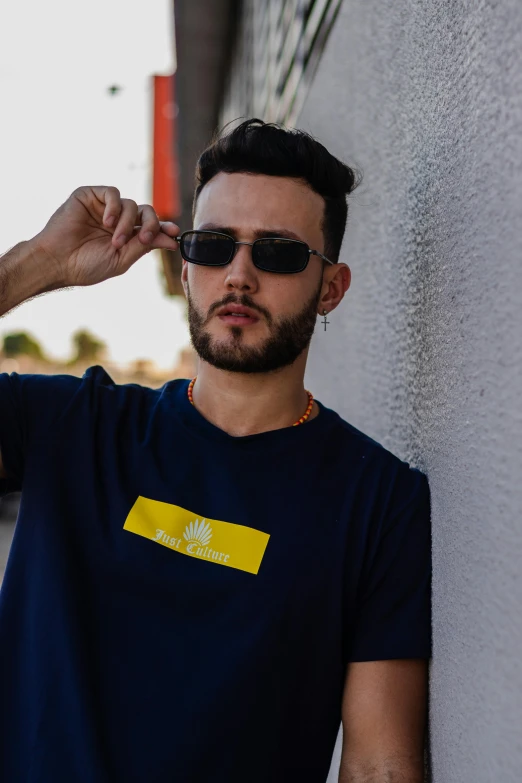 a man wearing sunglasses leaning against a wall, inspired by Raphaël Collin, featured on reddit, colors with gold and dark blue, wearing a marijuana t - shirt, official store photo, promotional image