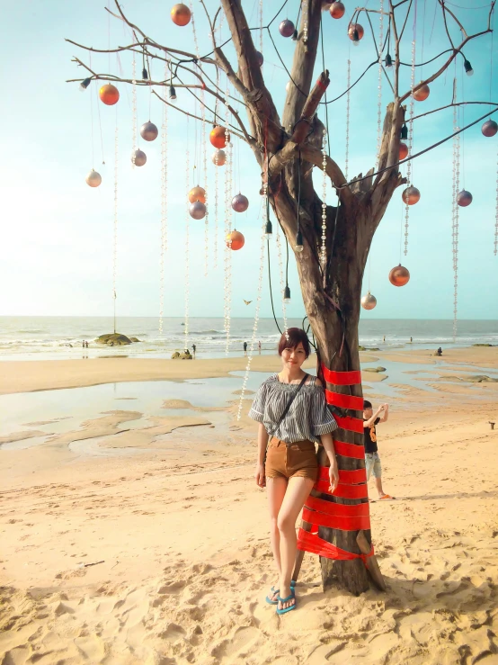 a woman standing next to a tree on a beach, hight decorated, holiday vibe, kuntilanak on tree, 🚿🗝📝