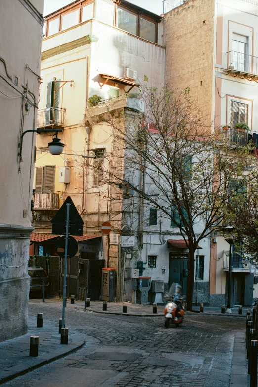 a person sitting on a bench on a cobblestone street, by Anita Malfatti, palermo city street, distant photo, single building, riding a motorbike down a street