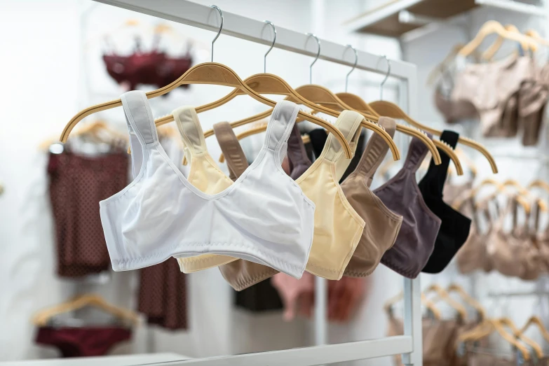 a variety of bras hanging on a rack in a store, a cartoon, by Adam Marczyński, trending on pexels, renaissance, wearing a crop top, manuka, brown, wearing white cloths