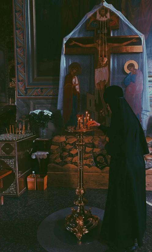 a woman in a black robe lighting a candle in a church, inspired by Elsa Bleda, orthodox, square, low quality photo, gif