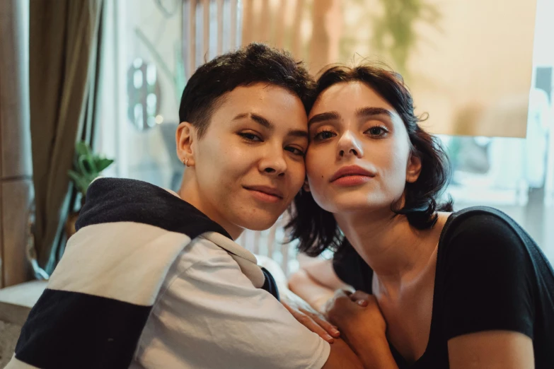 a couple of women sitting next to each other, trending on pexels, antipodeans, androgynous face, lesbian embrace, ayanamikodon and irakli nadar, short brown hair and large eyes