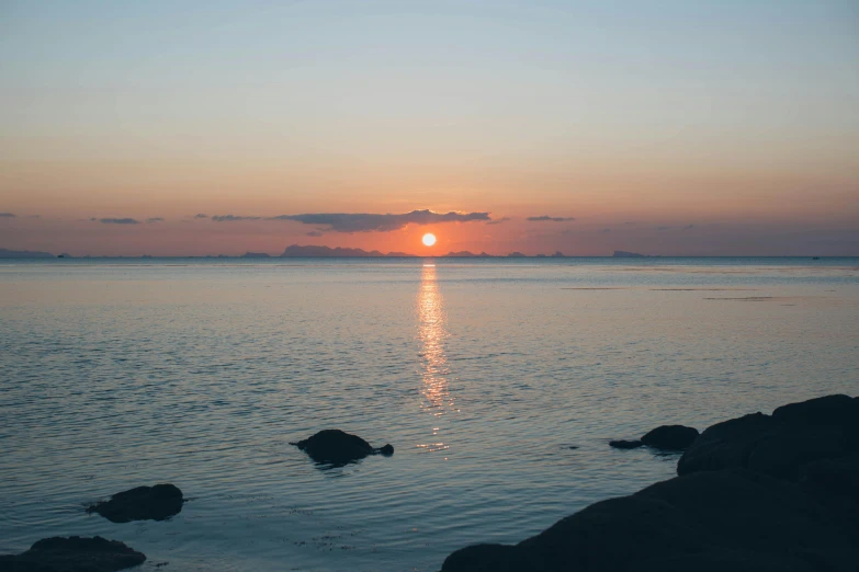 a sunset over a body of water with rocks in the foreground, cloudless-crear-sky, islands on horizon, high-quality photo, nina tryggvadottir