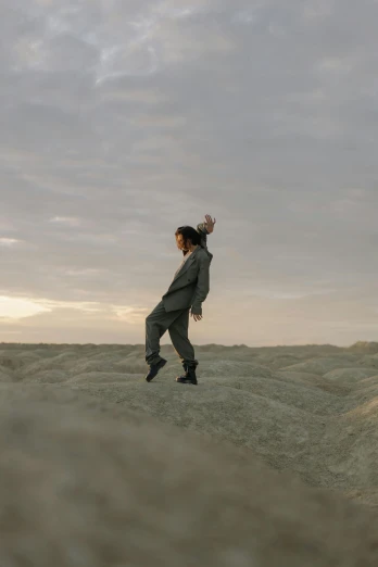 a man flying a kite on top of a sandy beach, an album cover, inspired by Scarlett Hooft Graafland, unsplash, wearing human air force jumpsuit, standing on rocky ground, evening at dusk, woman posing