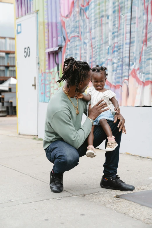 a woman squatting down while holding a child, a photo, by Washington Allston, trending on unsplash, black arts movement, handsome man, in new york city, multicolored, teaching