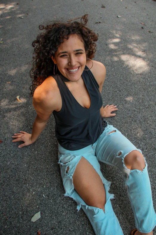 a woman sitting on the ground next to a skateboard, by Washington Allston, dark short curly hair smiling, wearing a low cut tanktop, estefania villegas burgos, view(full body + zoomed out)