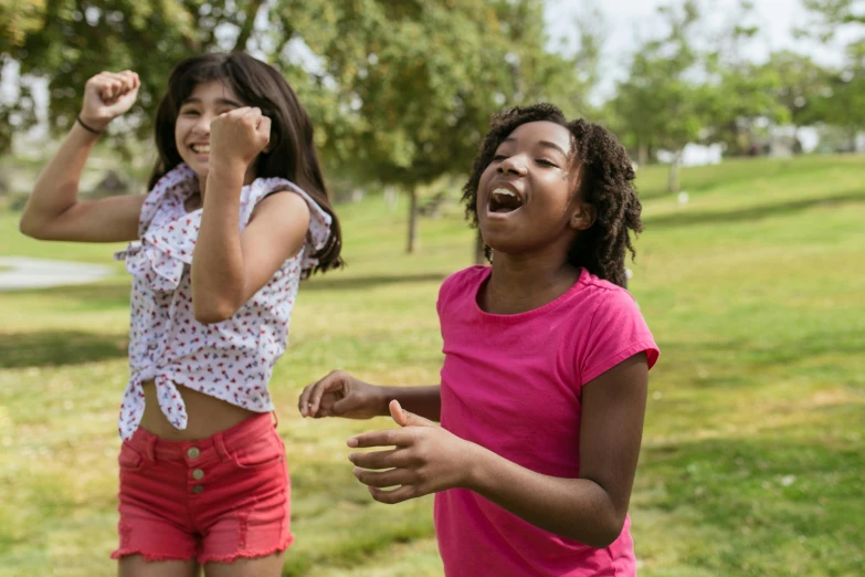 a couple of girls standing on top of a lush green field, pexels, happening, playing games, she is smiling and excited, ( ( dark skin ) ), actors