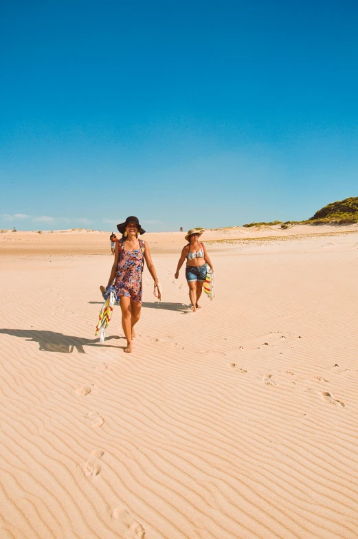 a couple of women walking across a sandy beach, surfing, beach on the outer rim, on the beach at noonday, vibe