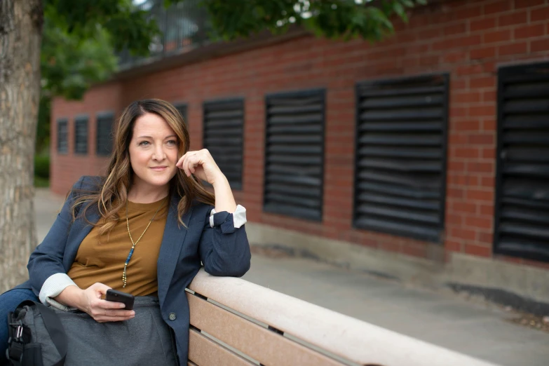 a woman sitting on a bench next to a tree, happening, smart casual, genevieve o'reilly, holds a smart phone in one hand, avatar image