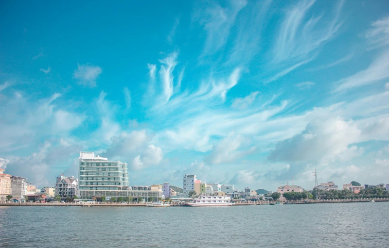 a large body of water with buildings in the background, pexels contest winner, guwahati, light blue sky with clouds, thumbnail, harbour