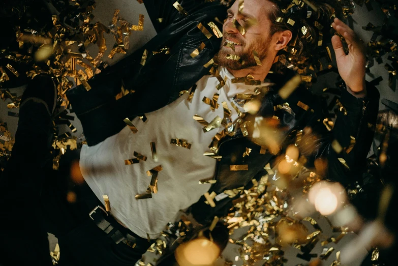 a man laying on top of a pile of gold confetti, by Julia Pishtar, pexels contest winner, leather clothing, avatar image, charlie day, michael fassbender
