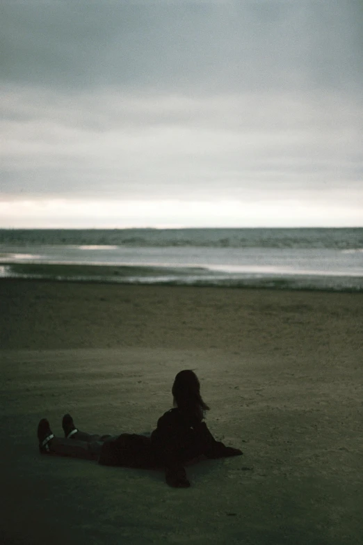 a person laying on a beach next to the ocean, inspired by Elsa Bleda, romanticism, overcast dusk, vsco, sittin