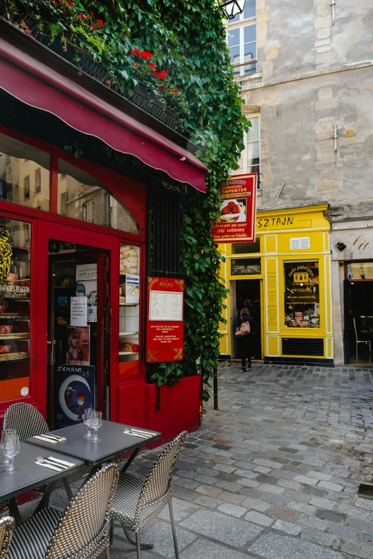 a couple of tables that are outside of a building, by Bernard D’Andrea, pexels contest winner, yellow and red color scheme, fresh bakeries in the background, french kiss, cobblestone street
