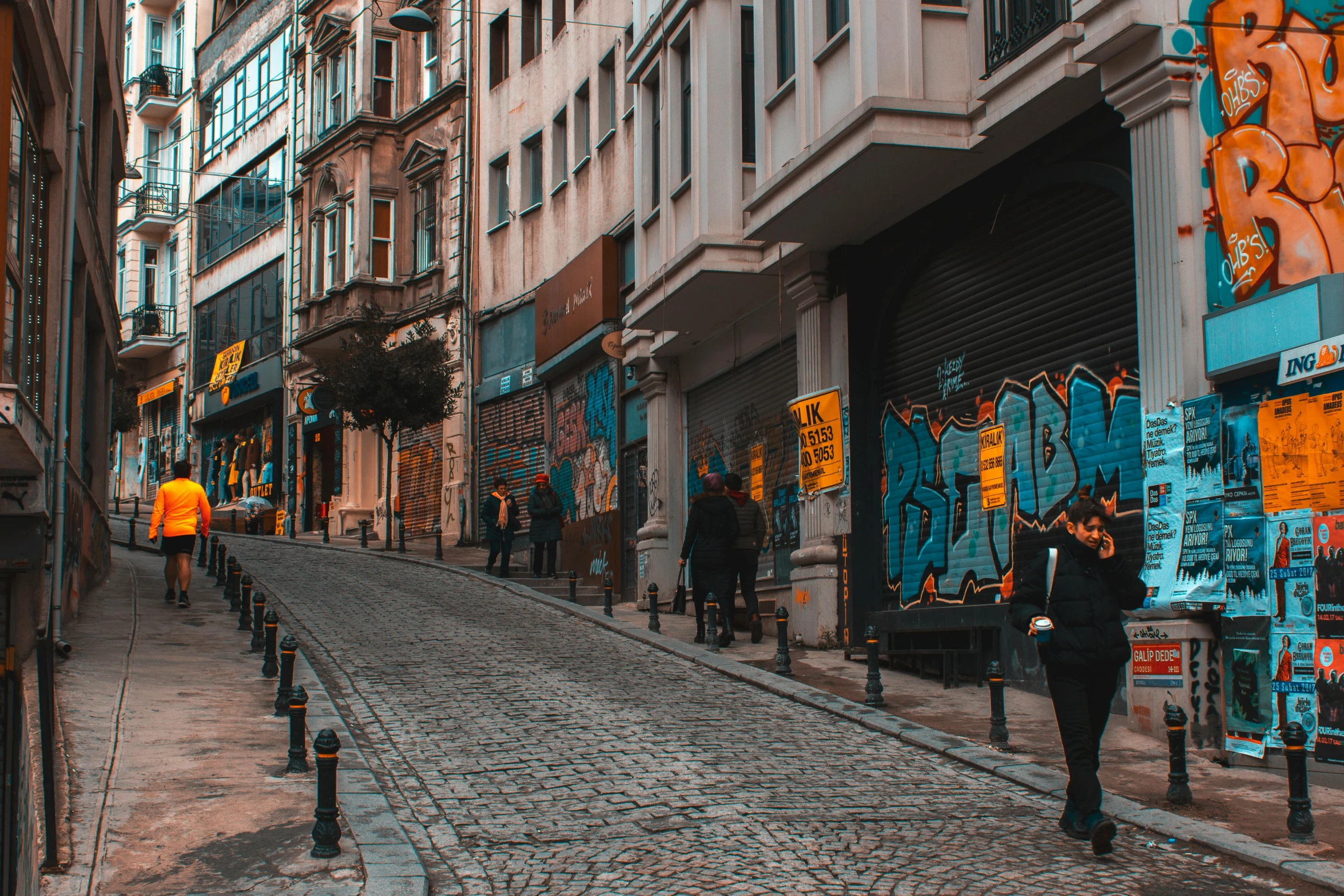 a person walking down a cobblestone street, inspired by Elsa Bleda, pexels contest winner, street art, fallout style istanbul, sao paulo in the year 2 0 7 0, storefronts, 90's photo