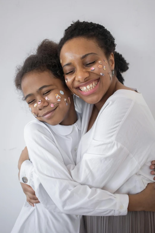 a couple of women standing next to each other, by Lily Delissa Joseph, pexels contest winner, markings on her face, happy family, wearing white pajamas, on a white background