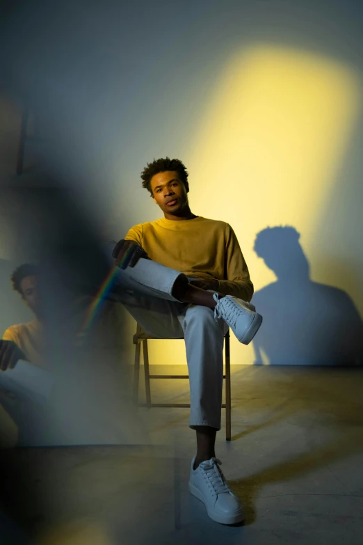 a man sitting on a chair in a room, an album cover, pexels contest winner, black teenage boy, portrait casting long shadows, yellow lighting from right, neutral pose