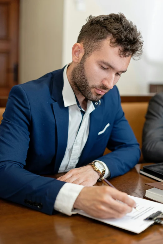 two men sitting at a table with papers and laptops, trending on unsplash, wearing dark blue suit, lgbtq, photo of a model, looking to his left