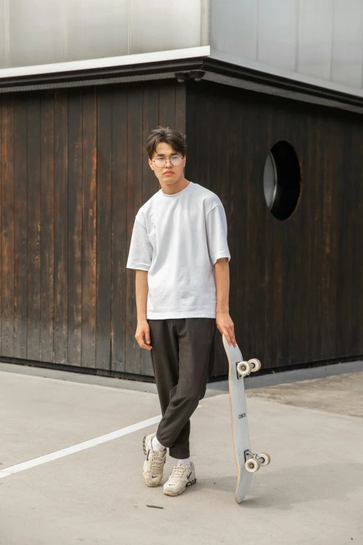 a young man holding a skateboard in front of a building, by Jang Seung-eop, plain white tshirt, grey, baggy black pants, japanese collection product