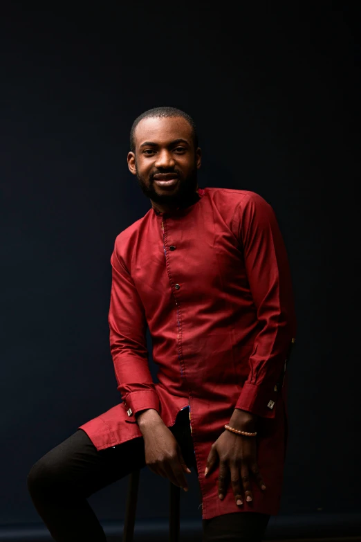 a man in a red shirt sitting on a chair, inspired by Ras Akyem, wearing red formal attire, david uzochukwu, dark backdrop, thumbnail