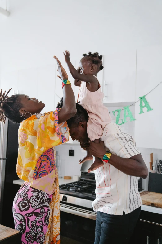 a woman holding a child on her shoulders in a kitchen, pexels contest winner, black arts movement, photograph of three ravers, lupita nyong'o, couple dancing, dwell