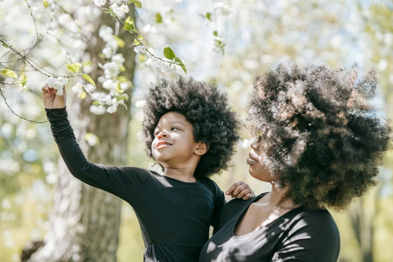 two women standing next to each other in front of a tree, by Dan Frazier, pexels contest winner, natural hair, with a kid, blossoming rhythm, black