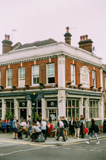 a group of people standing outside of a building, in a pub, victorian architecture, brick building, summertime