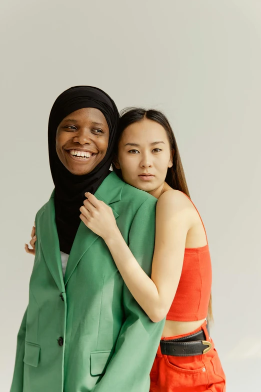 a couple of women standing next to each other, mix of ethnicities and genders, wearing green, arm around her neck, modelling