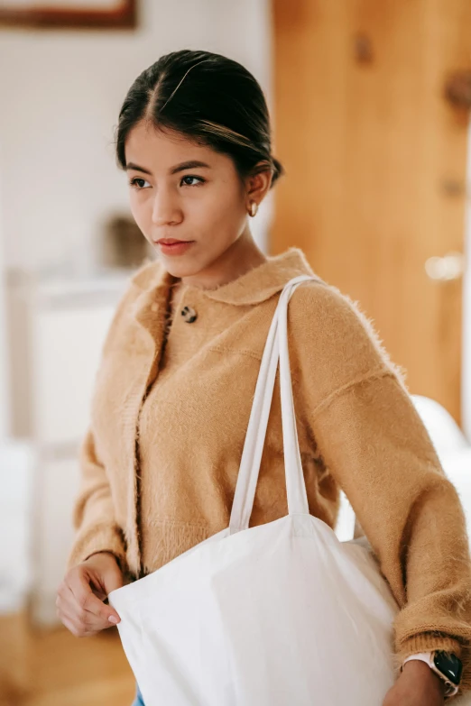 a woman in a brown sweater holding a white bag, inspired by Ruth Jên, pexels contest winner, south east asian with round face, linen, shopping groceries, white clothes