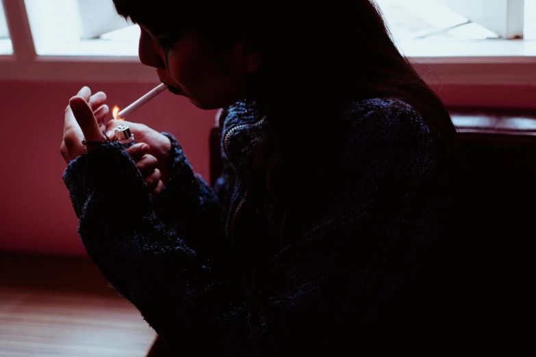 a woman smoking a cigarette in front of a window, inspired by Elsa Bleda, pexels contest winner, black haired girl wearing hoodie, lit up in a dark room, smoking a bowl of hash together, profile image